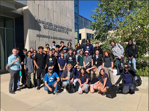  A group of high school students and chaperones stand outside the Advanced Manufacturing Sciences Institute, Aerospace & Engineering Sciences building on a sunny day. They appear to be on a field trip.