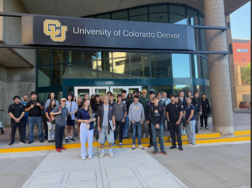 A group of students and adults stand outside a building with a large sign that reads University of Colorado Denver above the entrance. They are posed for a group photo.