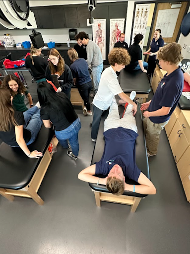 A group of students is busy in a sports medicine class, practicing injury evaluation and taping techniques on each other using training tables.