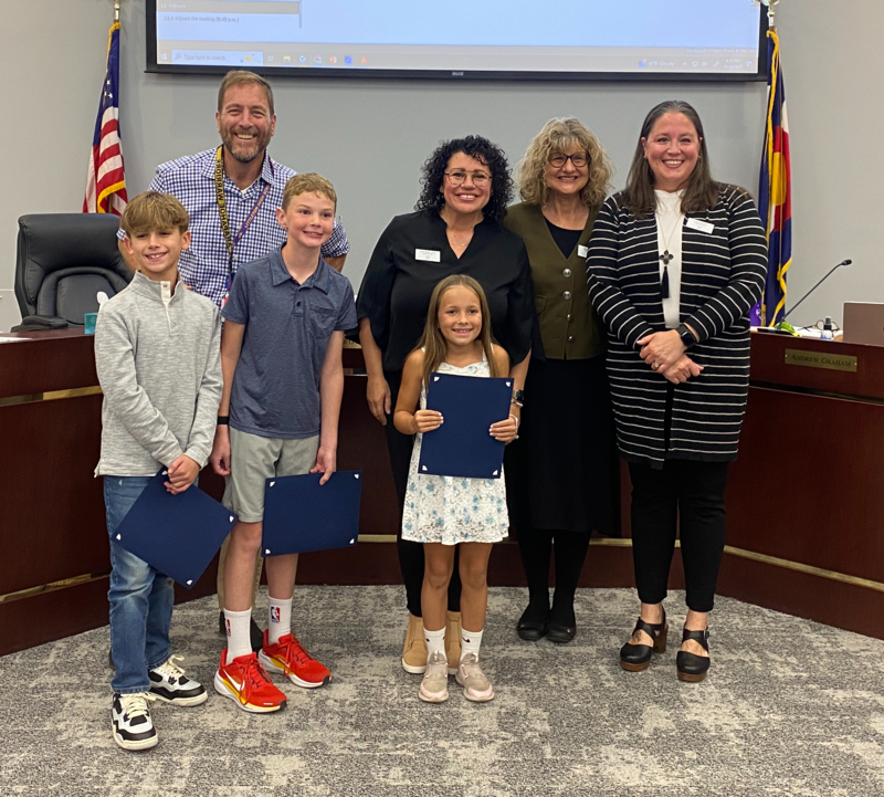Three students from Wilder Elementary stand with Board of Education members in the LPS Boardroom.