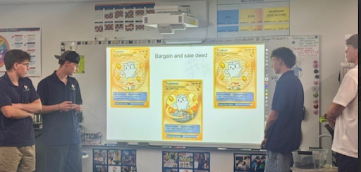 Four young men presenting in a classroom, showing a slide with "Bargain and sale deed" and illustrated trading card images.