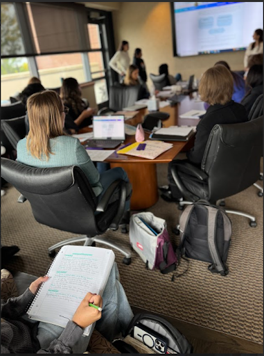 A close-up of a student taking notes in a notebook during a meeting in a conference room.