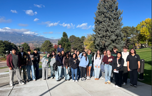 A large group of students is posing for a photo outdoors on a sunny day with a mountain and trees in the background.