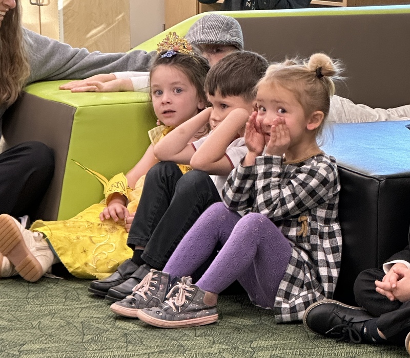 Children sit in a group story session learning about emotions and singing to bring in their puppet friend.