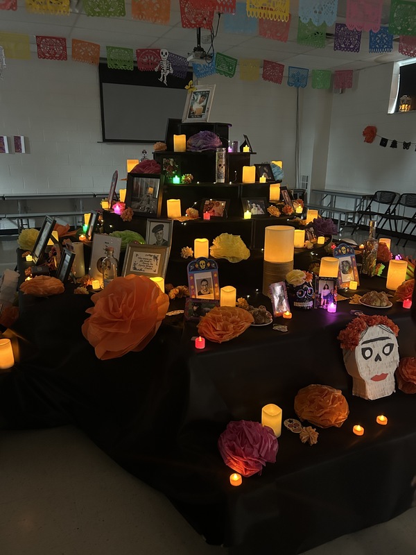 A large, tiered ofrenda (altar) covered in electric candles, photos, and paper flowers for Día de Muertos.