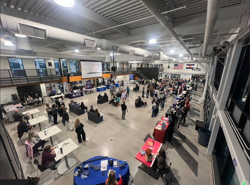 An aerial view of a busy, large event space with numerous attendees, tables, and booths set up for an expo or career fair.
