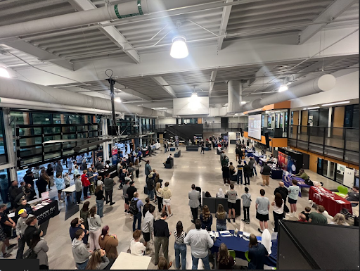 An overhead view of a large, well-lit indoor event with many attendees gathered around booths for an aerospace or industrial career night.