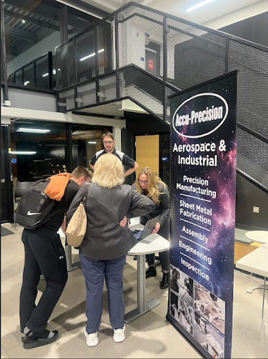 A group of people interacting with representatives at a small booth next to a pull-up banner advertising Accu-Precision Aerospace & Industrial services.