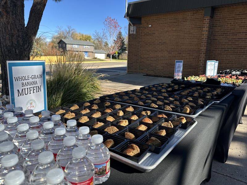 A table displaying many whole-grain banana muffins and bottled water at an outdoor event.