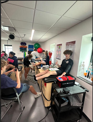 Students practicing sports medicine techniques, including using a Game Ready compression system, in a bright physical therapy or classroom lab.