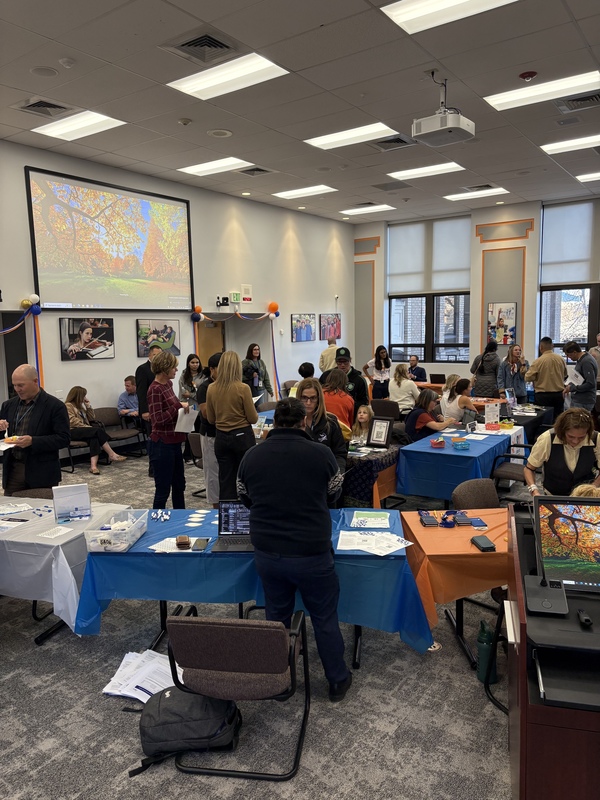 People gather at an event with tables covered in blue and white cloths and a nature scene projected on a screen.