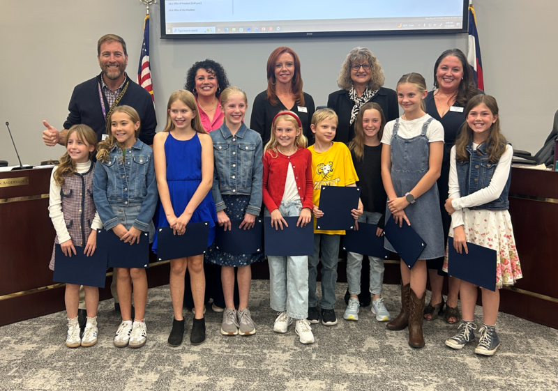 Elementary students and adults pose holding certificates after being honored at a school board meeting.