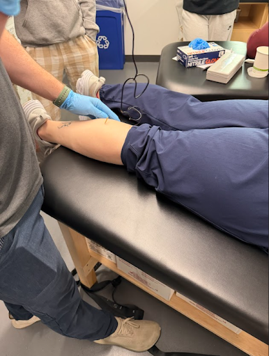 Close-up of a student applying an electrode to another student's leg on a treatment table.