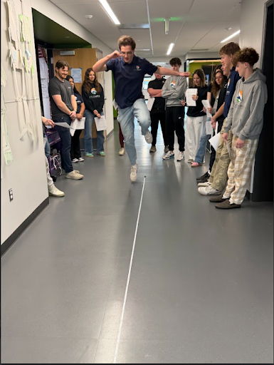 Student jumps over a white line in a hallway as peers watch from the side.