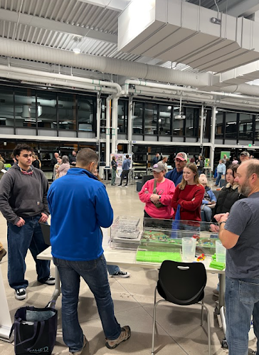 People gather around a table with exhibits in a large, well-lit modern building space.