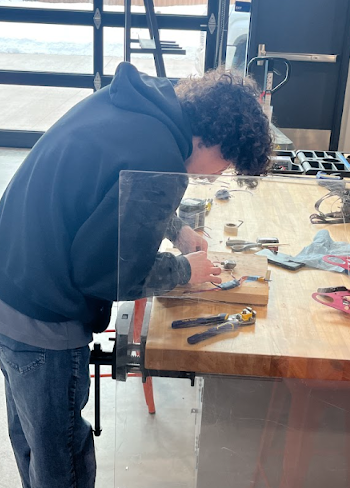 A student works on wiring components on a workbench in a brightly lit lab.