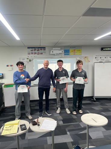 An older man shakes hands with one of three students holding certificates in a classroom