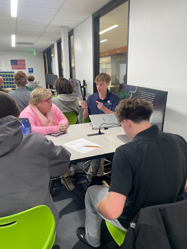 A student presents a display on a laptop screen to a woman and another student at a table.