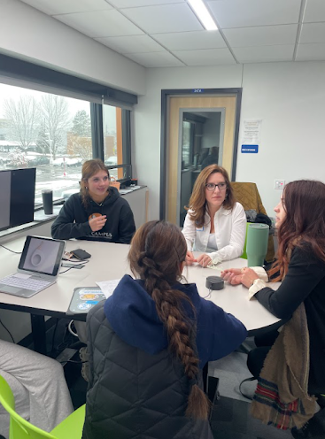 Four women sit at a round table, discussing a topic by a window with a snowy view.