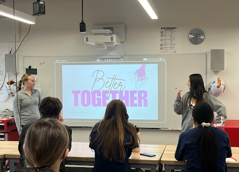 Two students present a slide titled "Better Together" to a seated audience in a bright workshop space.