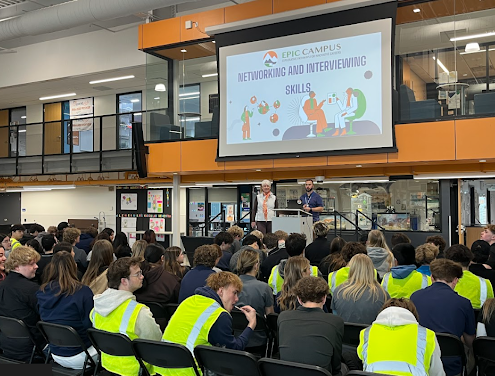 A large group of students in a modern atrium attends a presentation titled "Networking and Interviewing Skills."