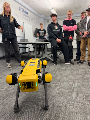Students watch a demonstration of a yellow four-legged robotic dog in a modern technology lab.