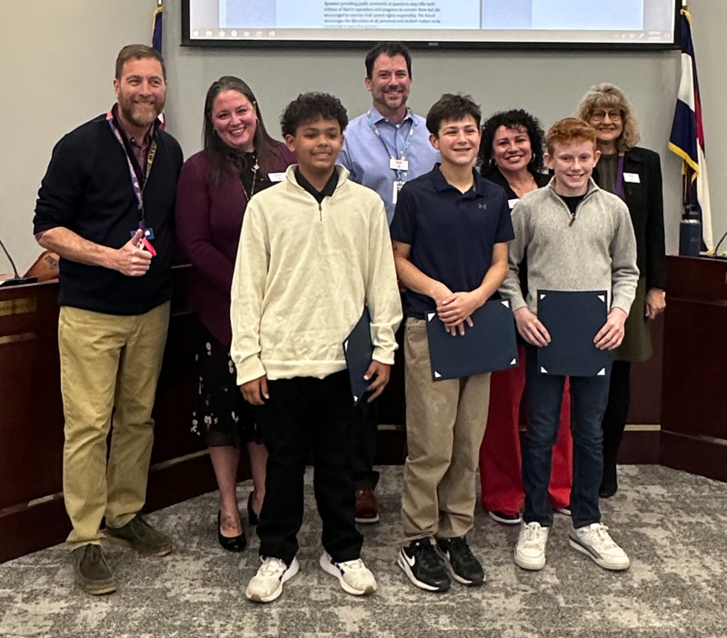 Three students stand with Littleton Public Schools board members holding award certificates during Student Spotlight at the Board meeting.
