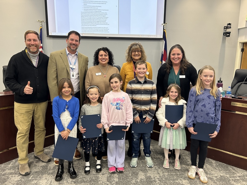 Six elementary students and five Board of Education members pose together with certificates at a meeting.