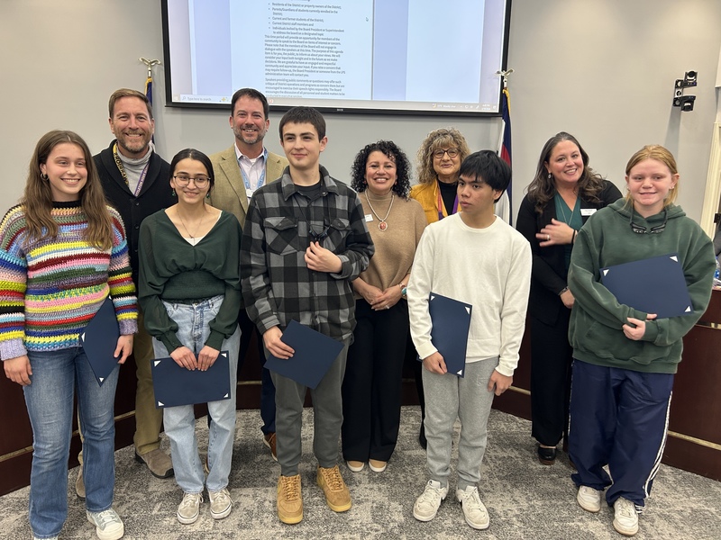 Five secondary students stand with five Board of Education members while holding award certificates.