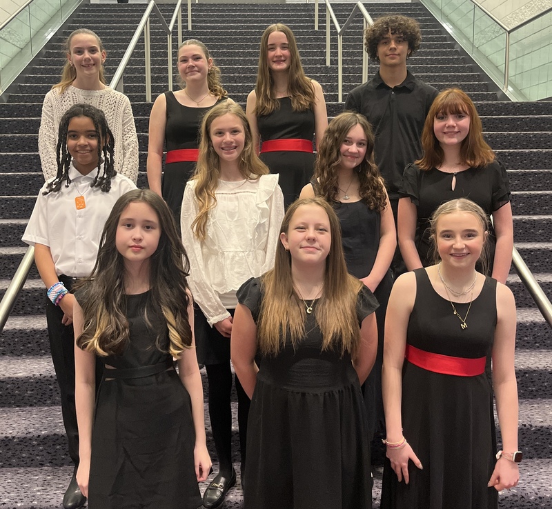 A group of ten students in formal black and white performance attire poses on a wide indoor staircase.