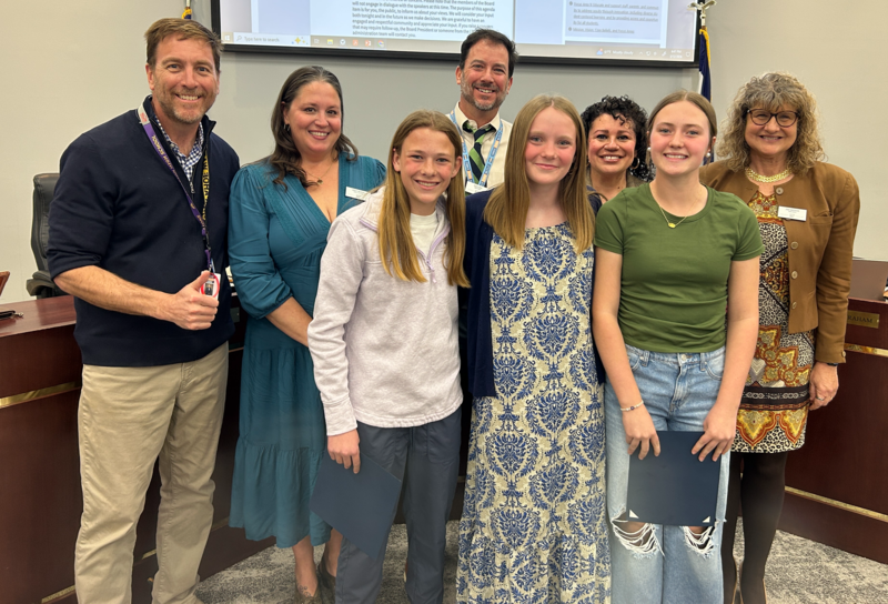 Three female middle school students stand with the LPS Board of Education during the Student Spotlight segment of the Board of Education meeting.