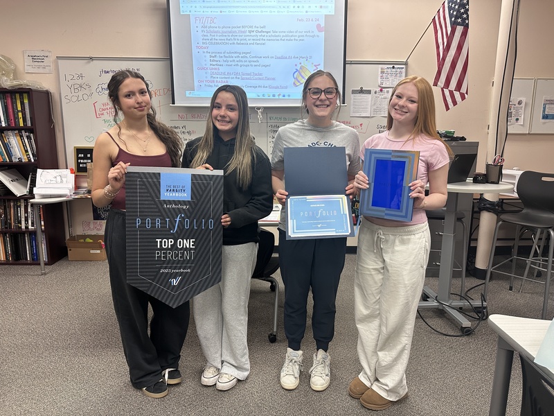 Four female students hold up yearbook awards in a classroom.