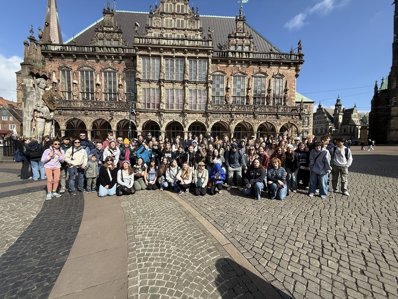 Large student group poses in a cobblestone plaza in front of the ornate, historic Bremen Town Hall in Germany.