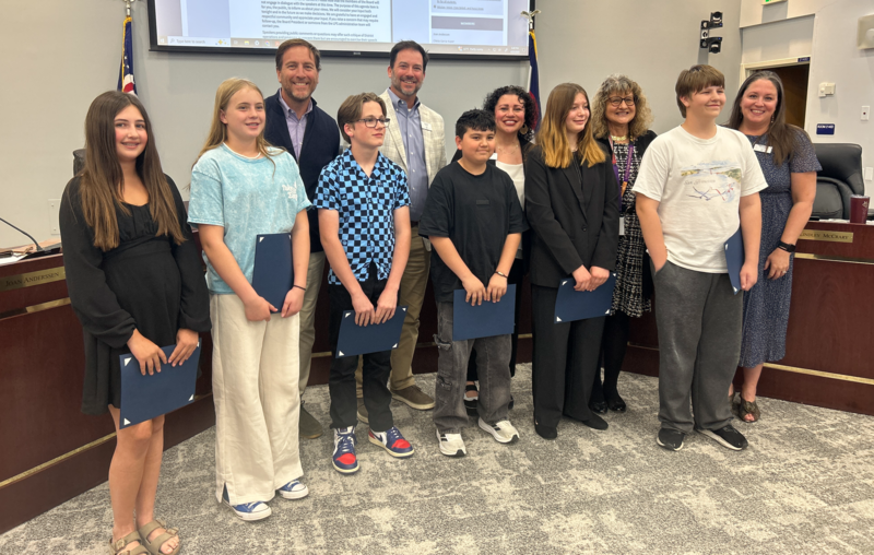 Middle school students stand in a row with certificates, posing for a photo with school board members.