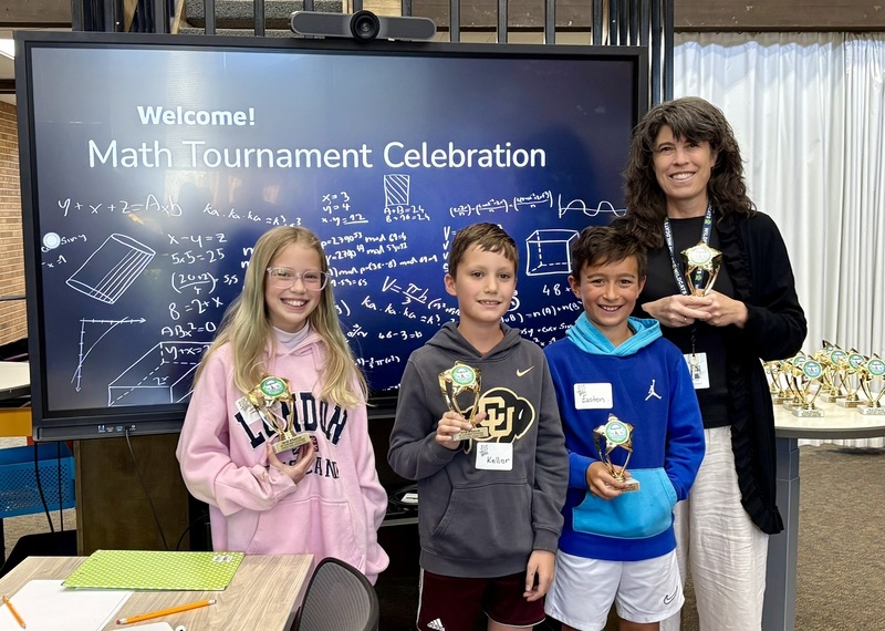 Three Wilder Elementary 4th graders and a teacher holding trophies in front of a Math Tournament Celebration screen.