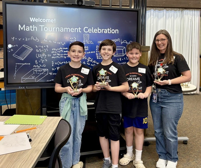 Three Ford Elementary 4th graders in matching black shirts pose with trophies and their teacher at a math event.