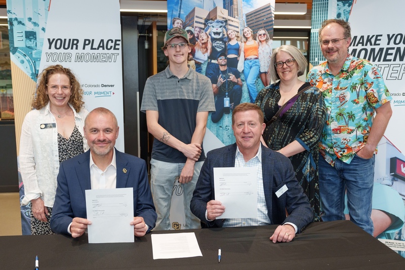 Six people posing behind a table with signed documents and University of Colorado Denver banners in the background.