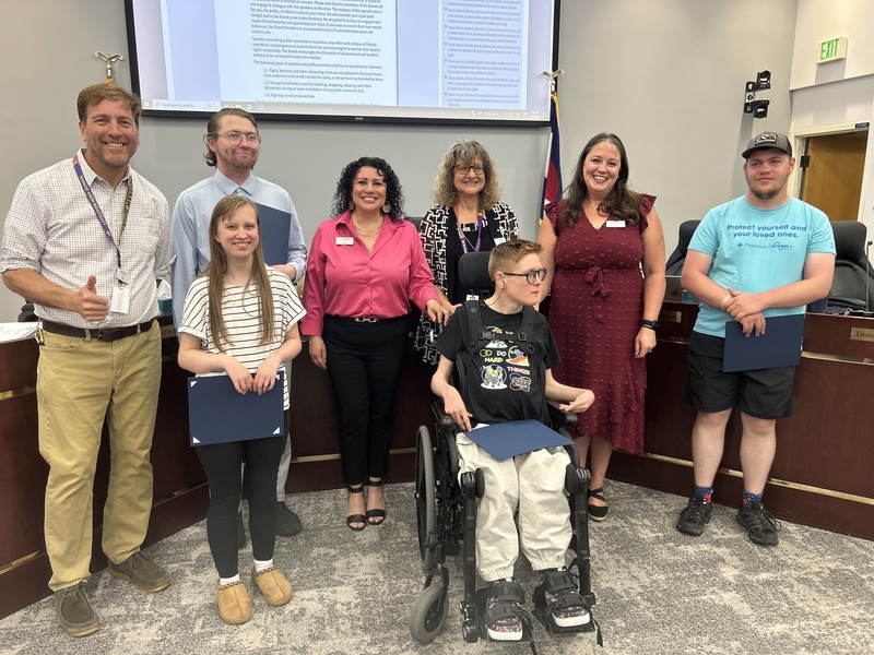 Four high school students, including one in a wheelchair, pose with their recognition folders and LPS board members.