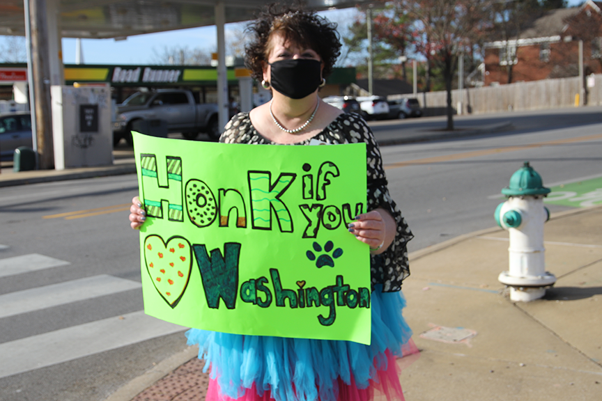 Assistant Principal at Washington Elementary holds sign Honk if you Love Washington. She agreed to do this if Washington students met their goal for their food drive and Socktober event. Five hundred boxes of mac and cheese were collected for the district food pantry and 200 pairs of socks for the Seven Hills Day Center. 