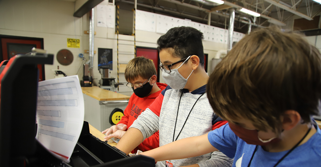 Masked students working together on robotics project in engineering class.