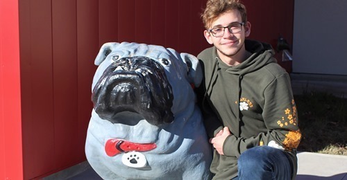 Photo Credit: Bartlesville Examiner Enterprise. Mikey Bradley pictured with bullpup statue in front of high school entrance.
