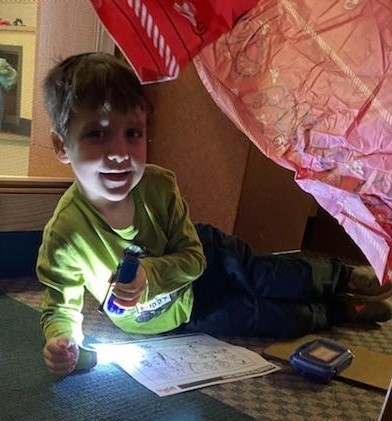 Young boy uses flashlight to work in a tent in library