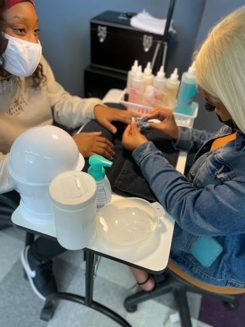 2 students sitting across from each other, while one practices her manicure skills. 