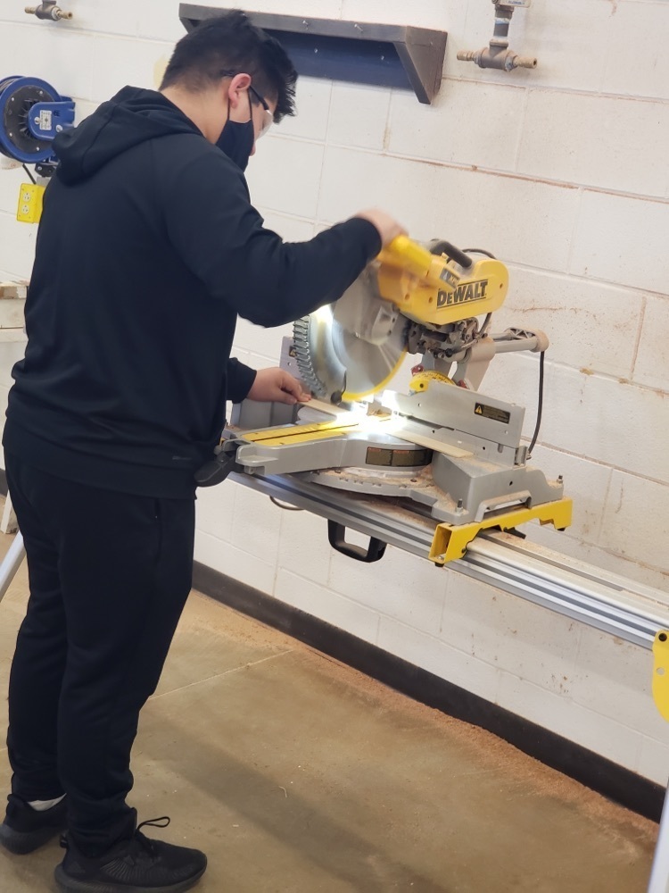 Student using a cutting machine to cut wood. 