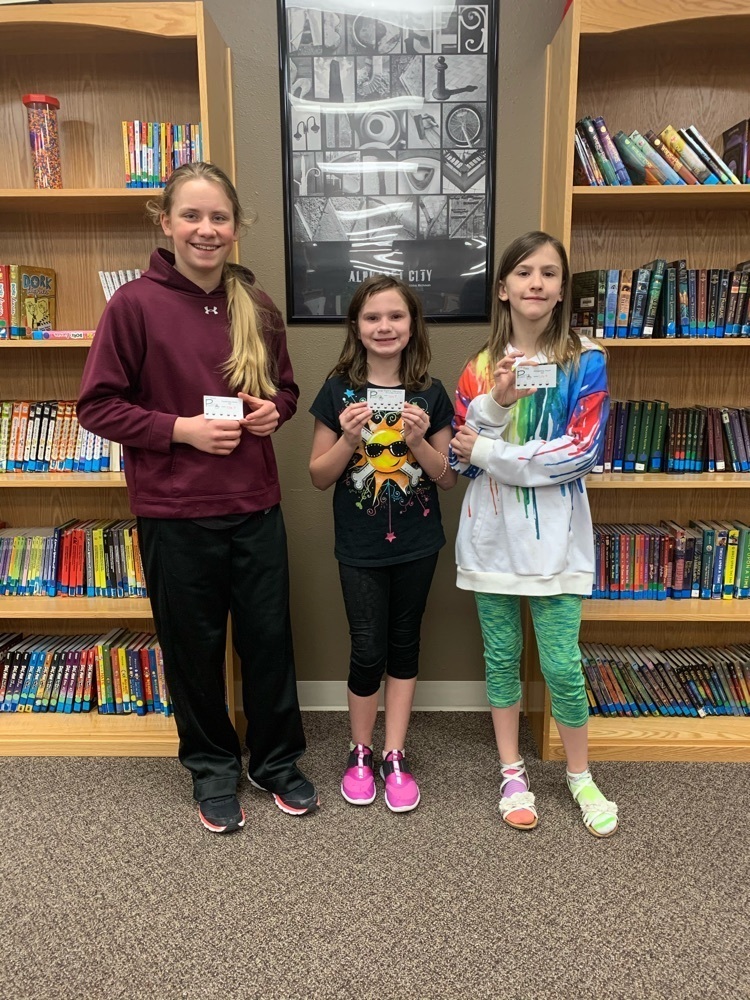 3 girls standing near book shelves holding their prizes from winning first, second, and third place in a typing tournament.