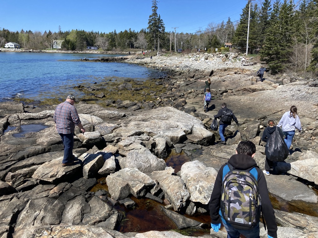 8th grader walk along a rocky shore picking up trash