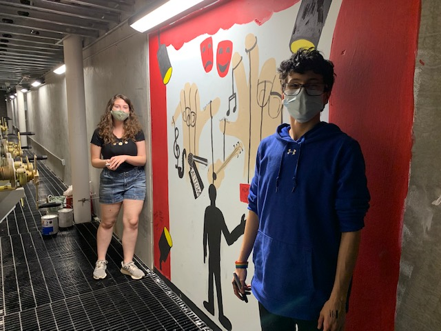 two students standing by a mural 