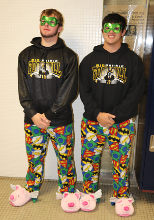 Two students celebrating twin day with superhero pants, pig slippers, green masks and football sweatshirts