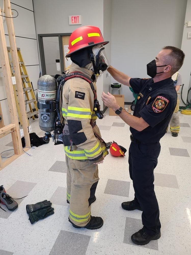 teacher working with student to put in fire gear