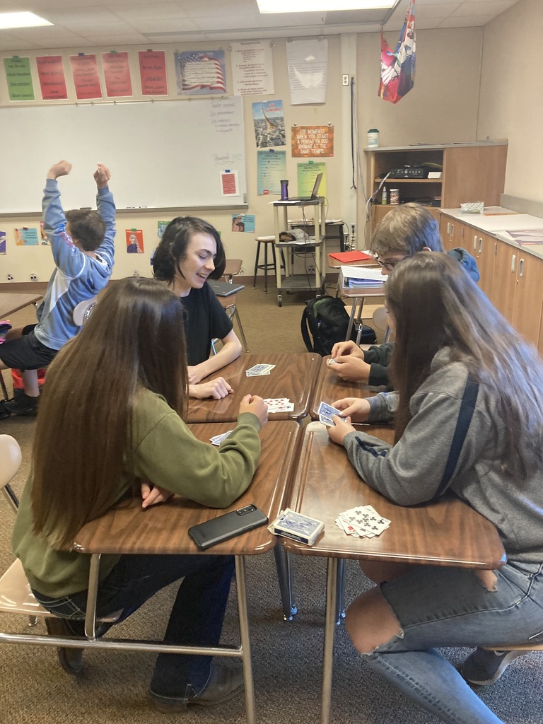 2 boys and 2 girls sitting in desks playing cards